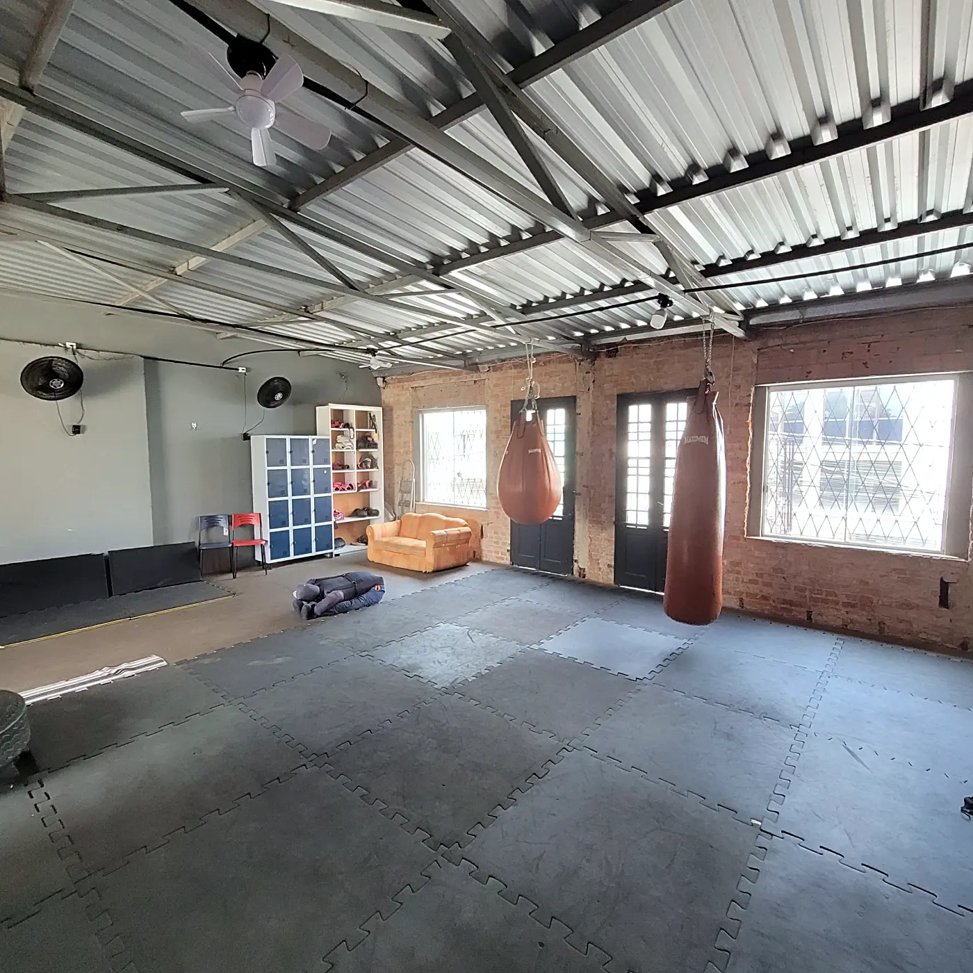 Área de boxe e muay thai com tatame, sacos de pancada e sofá laranja