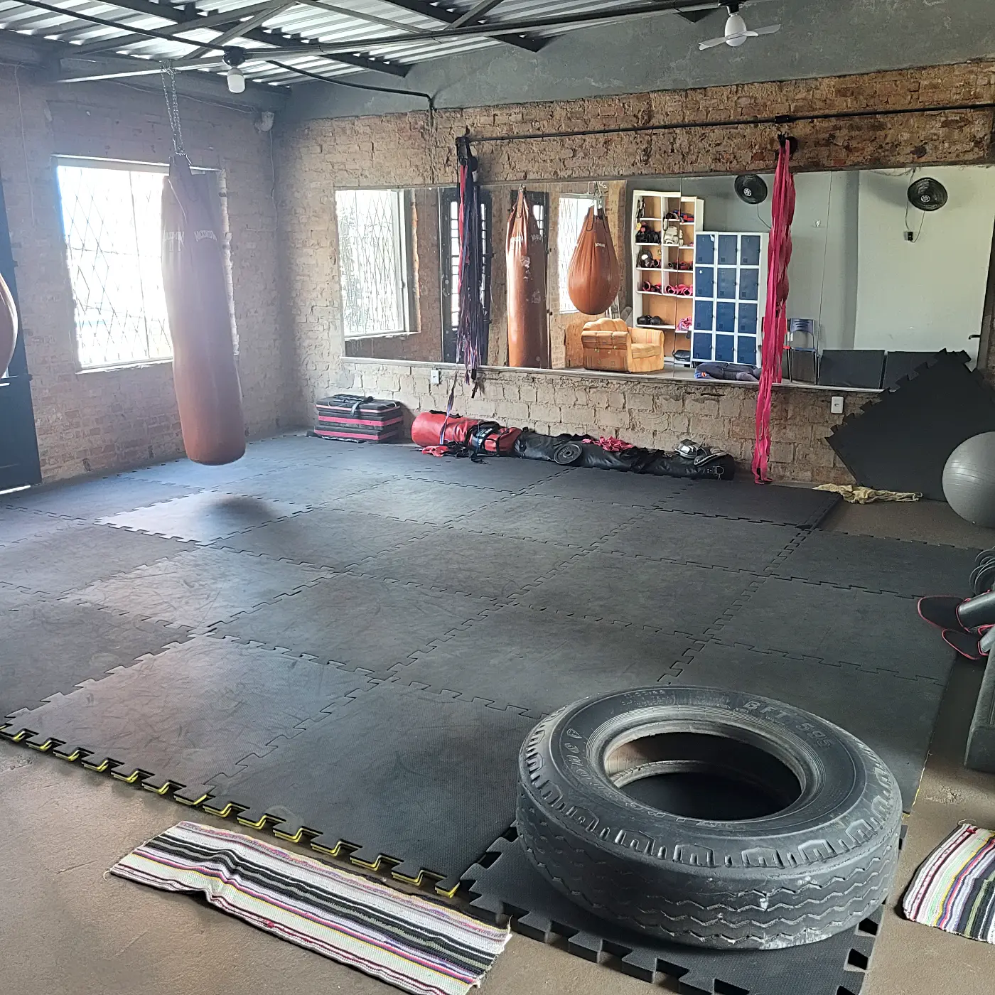 Tatame com pneu para treino e parede de tijolinho na área de muay thai