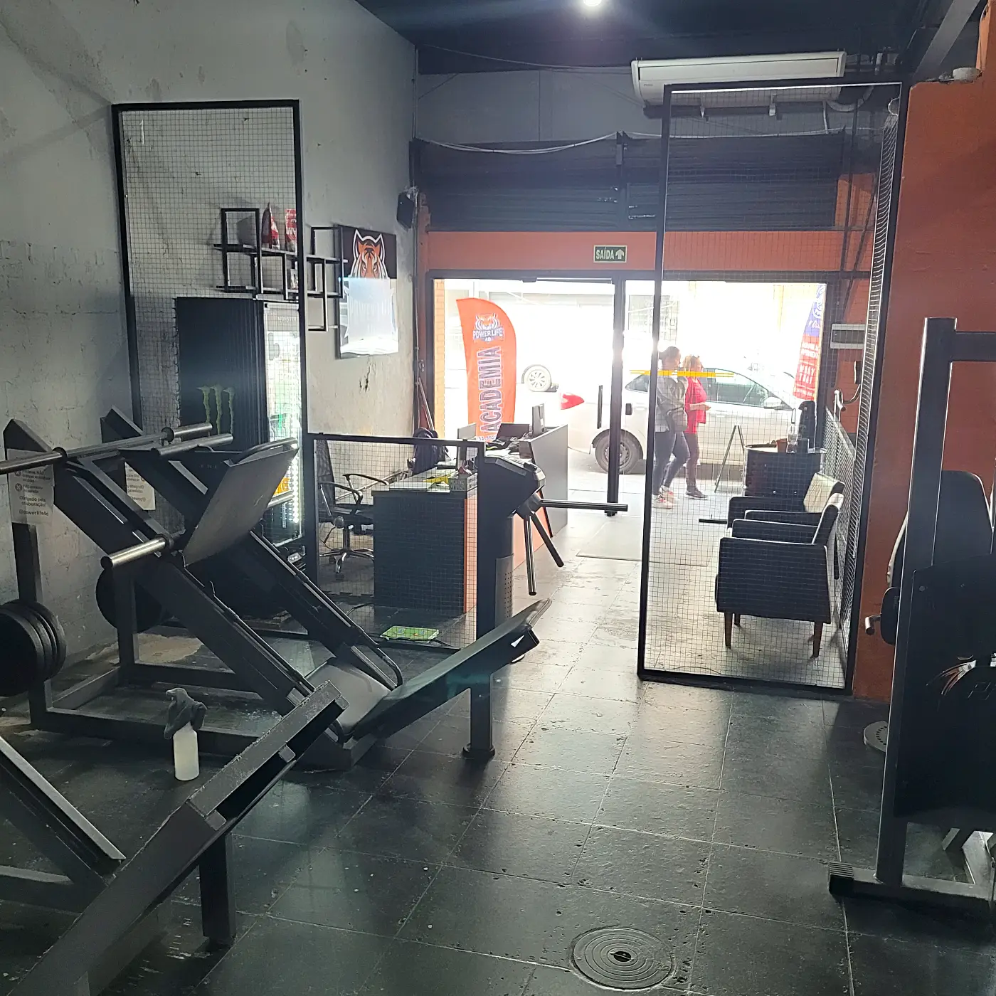 Entrada da academia vista de dentro, com catraca e poltronas de espera