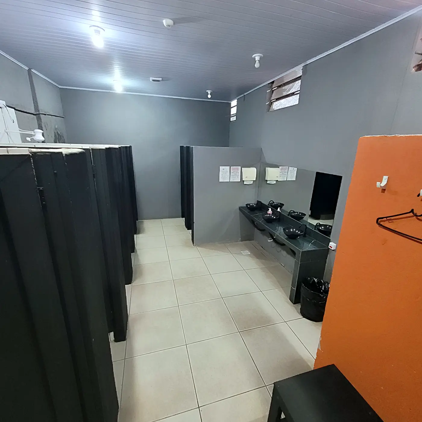 Vestiário da PowerLife 4D com boxes de chuveiro, bancada de pias e painel laranja