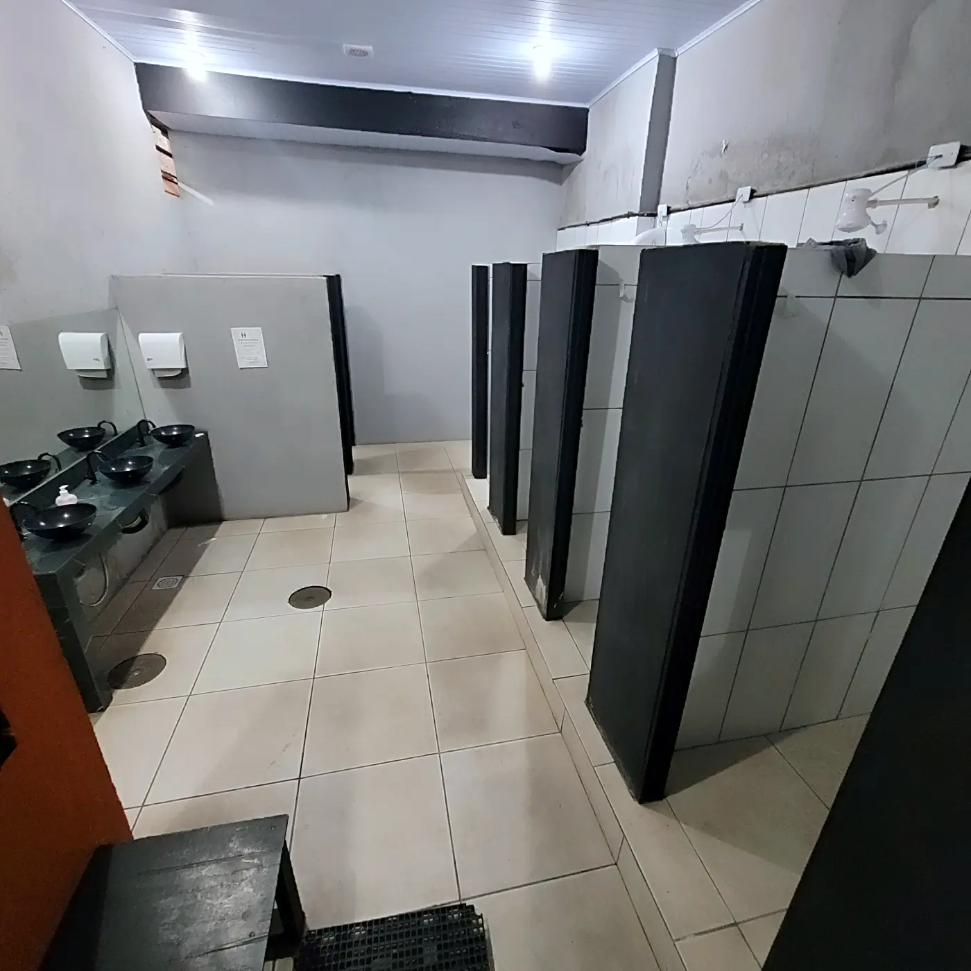 Vista ampla do vestiário com boxes de chuveiro à direita e bancada de pias ao fundo