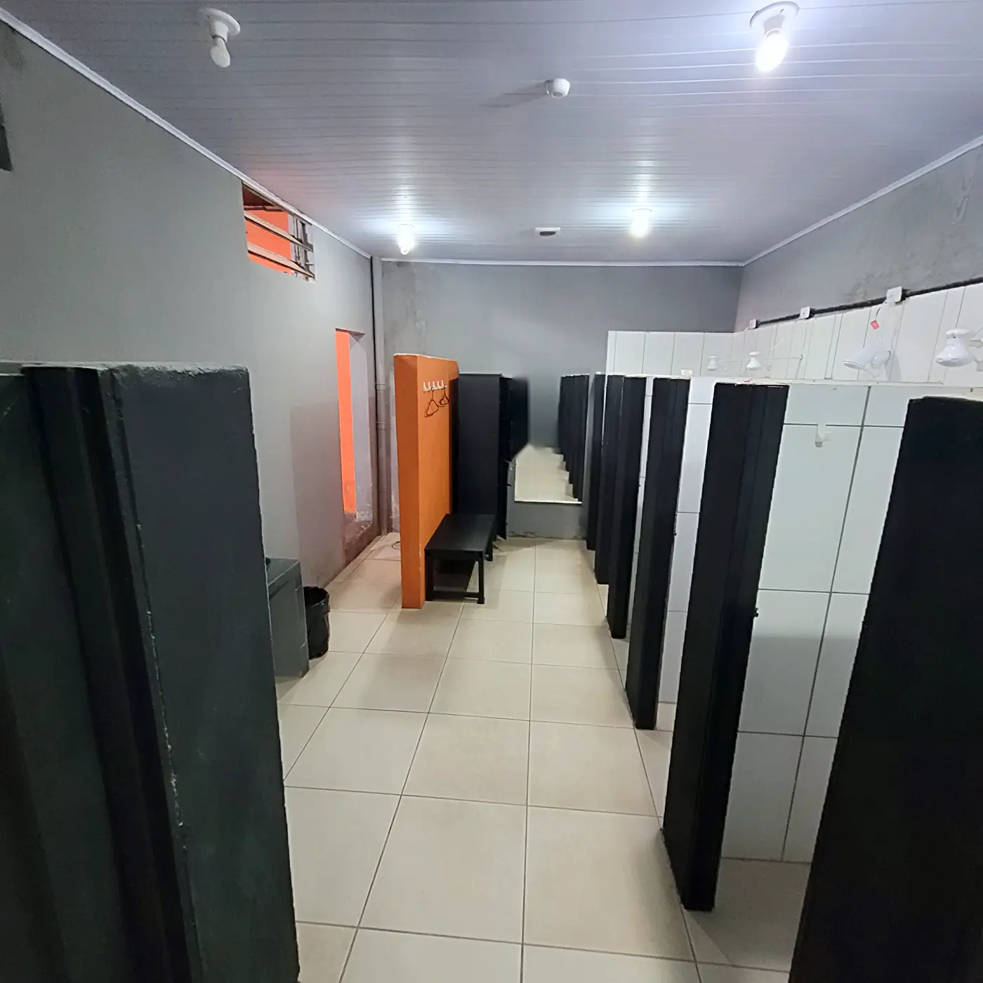 Corredor do vestiário entre os boxes de chuveiro, com banco e armário ao fundo